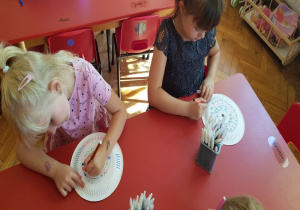 dzieci przy stoliku ozdabiają wzorami powierzchnię papierowego talerzyka rysując wzory mazakami